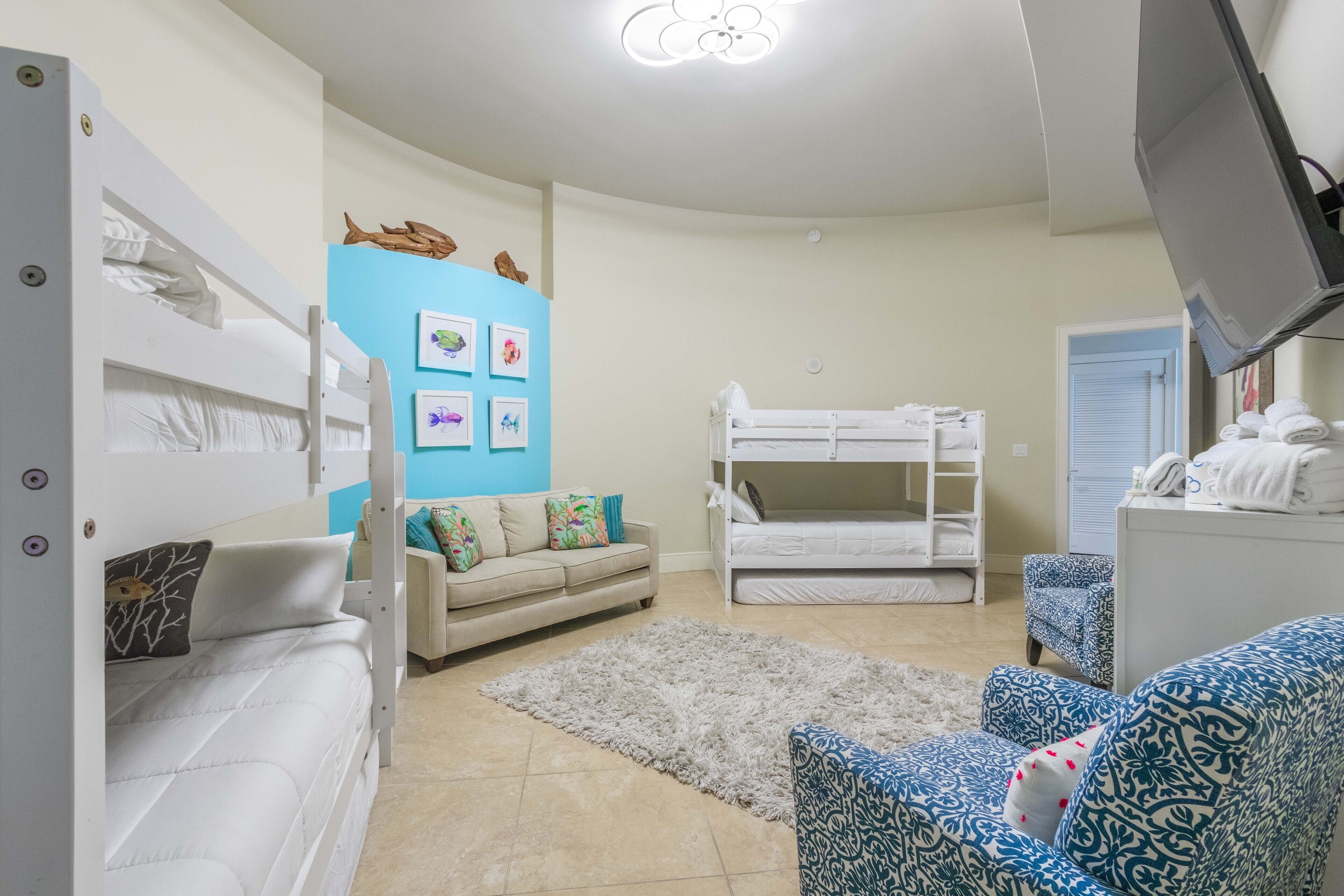 A compact living space with bunk beds, a sofa, patterned chairs, a blue accent wall, and framed pictures.