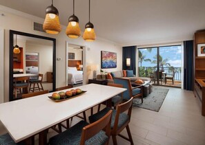 Relax in a stylish room with a dining area, sofa, and large window overlooking palm trees and the ocean.