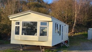 A small, single-story mobile home with a front porch and a ramp for accessibility. - Immaculate 2-bed Static Caravan Near the Lake (Millom)