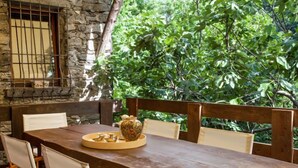 Uma mesa de madeira rústica com cadeiras, uma parede de pedra e uma janela com grades.