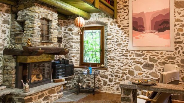 Um interior rústico de pedra com lareira, uma janela com vista e um quadro na parede.
