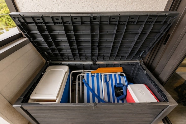 Uma caixa de armazenamento com uma estante de metal, um recipiente branco, uma mala azul e branca listrada e um objeto vermelho e branco.