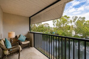 A balcony with wicker furniture, a lamp, and a view of a body of water with trees. - Park Shore Resort, Top Floor BLDGH #347-Lake view (Park Shore Resort)