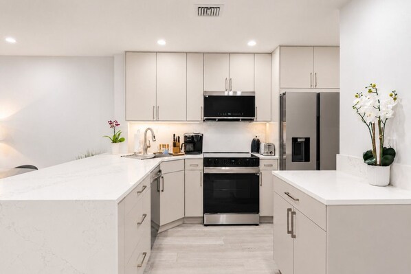 A modern kitchen with a central island, stainless steel appliances, and white cabinetry. - Park Shore Resort, Top Floor BLDGH #347-Lake view (Park Shore Resort)