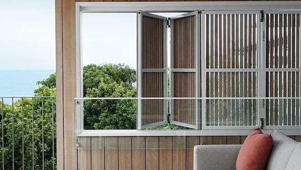 Ein moderner Außenbereich zum Sitzen mit einer Holzterrasse, einem weißen Tisch und einem grauen Sofa mit einem roten Kissen.