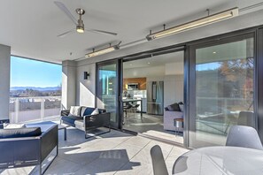 A modern balcony with a ceiling fan, a dining area, and a kitchen visible through glass doors.