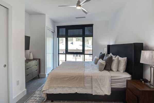 A bedroom with a bed, a nightstand, a dresser, a ceiling fan, and a large window.
