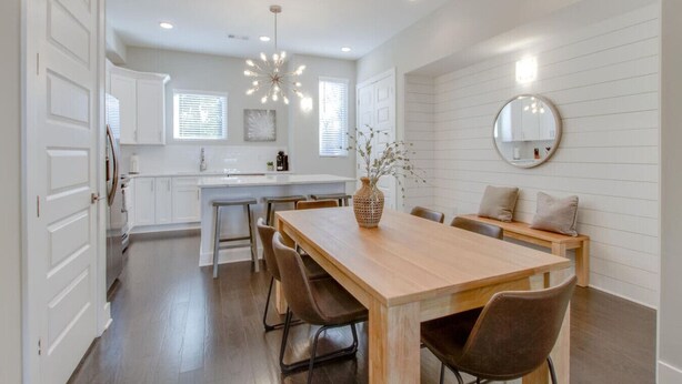A modern kitchen with white cabinetry, a central island, and a dining area with a wooden table and chairs.