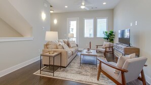 A modern living room with a sofa, coffee table, and chairs, a television, and a staircase.