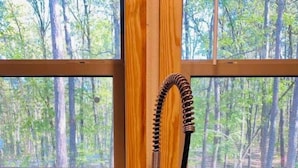 A stainless steel kitchen sink with a flexible hose faucet, set against a backdrop of a wooden window frame and a view of a forest. - Romantic Splash Brand New 1 Bedroom Efficiency Cabin, near Broken Bow Lake (Broken Bow)