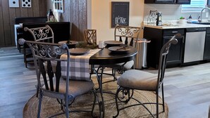 A dining area with a round table, chairs, and a woven rug. There is a kitchen in the background with dark cabinets and a window. - The Flippin Fisherman  (Flippin)