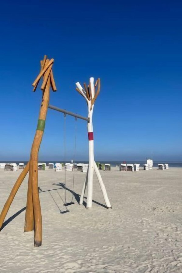 Una playa con una escultura de madera y estructuras blancas al fondo.