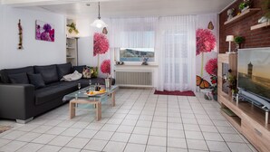A modern living room with a black sofa, a glass coffee table, and a TV on a wooden stand. - Knurrhahn by Interhome (Norddeich)