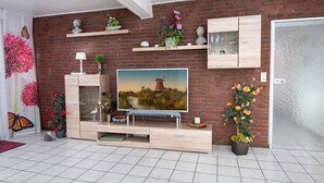 A modern living room with a brick wall, a flat-screen TV, wooden cabinets, and decorative items. - Knurrhahn by Interhome (Norddeich)