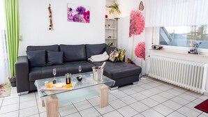A modern living room with a black leather sofa, a glass coffee table with remote controls, and a white radiator. - Knurrhahn by Interhome (Norddeich)