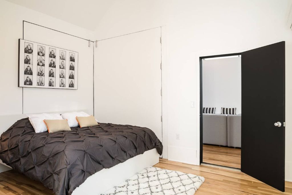A bedroom with a bed, a wall-mounted photo collage, a black door, and a view into an adjacent room with a white wardrobe.