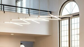 A modern interior with a suspended light fixture, large windows, and a staircase.
