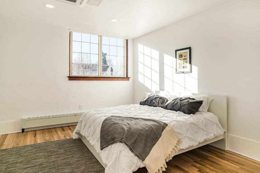 A bedroom with a bed, a window, and a framed picture on the wall.