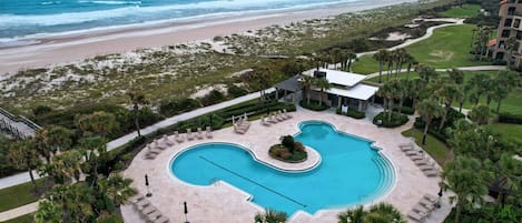 Un resort con una piscina amplia, acceso a la playa y palmeras.