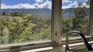 Une fenêtre donnant sur un paysage montagneux et une maison.