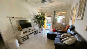 A living room with a flat-screen TV, a sofa, a coffee table, and a potted plant.