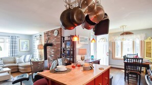 Una sala de estar acogedora con chimenea, un comedor con mesa de madera y una cocina con utensilios colgando.
