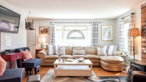 Una sala de estar con sofá, reposapiés, mesa de centro y televisor.
