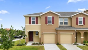 A two-story residential building with a beige exterior and red shutters, featuring two garage doors and a front entrance.