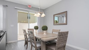 A dining area with a table, chairs, a chandelier, potted plants, and a mirror on the wall.