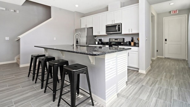 A modern kitchen with white cabinets, a central island with bar stools, a microwave, and a stainless steel refrigerator.