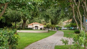 A paved pathway leading to a building with a tiled roof, surrounded by lush greenery and trees.
