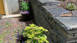 A garden with stone walls, various plants, and a wooden staircase leading to a building.