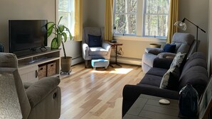 A living room with a flat-screen TV, two sofas, a coffee table, a ceiling fan, and a potted plant.