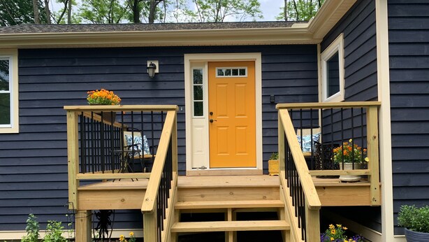 A two-story house with a wooden front porch, a yellow door, and a small window.
