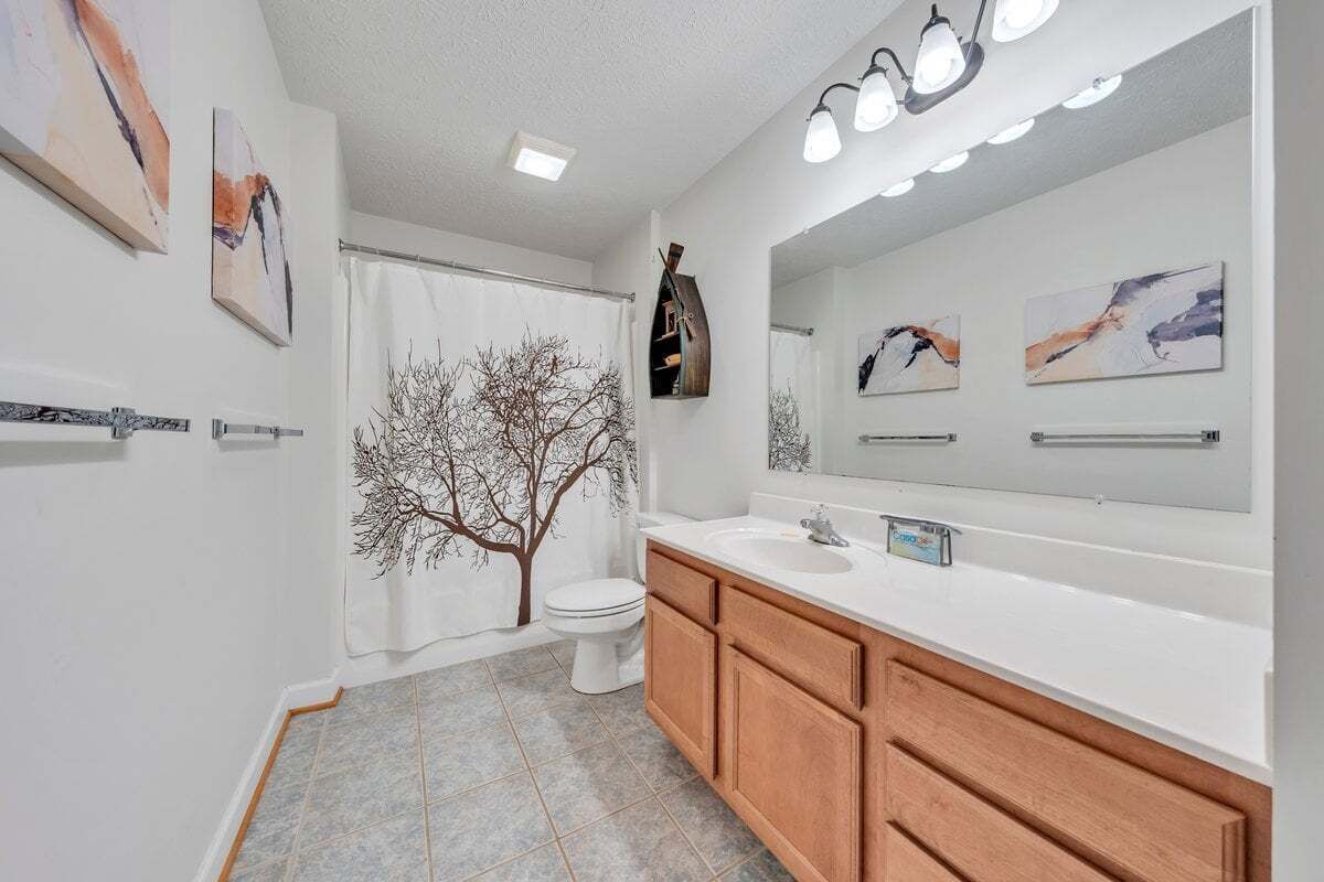 A bathroom with a white sink, wooden vanity, and a large mirror. There is a tree decal on the wall and a shower curtain with a tree design.
