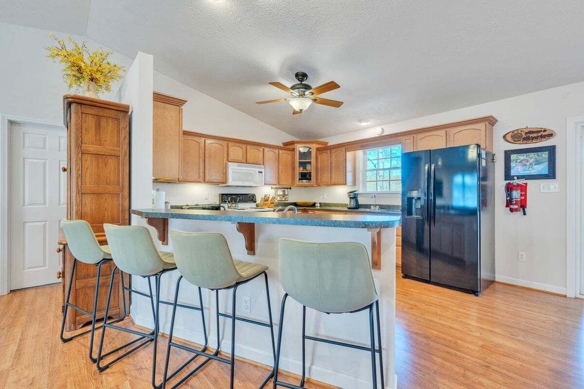 A kitchen with wooden cabinets, a black refrigerator, a bar stool area, and a ceiling fan.