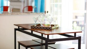 A kitchen with a wooden table, a tray with glassware, and a window with curtains.
