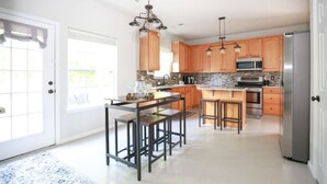 A modern kitchen with wooden cabinets, a central island with bar stools, stainless steel appliances, and a chandelier.