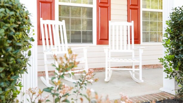 A porch with two white rocking chairs and red shutters.