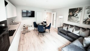 Un salon moderne avec un canapé gris, une table à manger avec des chaises bleues et un téléviseur à écran plat fixé au mur.