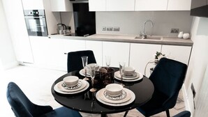 Une cuisine moderne avec des meubles blancs, un plan de travail noir et un coin repas comprenant une table ronde et des chaises bleu foncé.