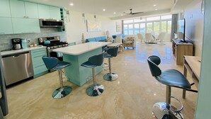 Cozinha moderna com armários verde-água, uma ilha central com banquetas e uma área de refeições com cadeiras brancas.
