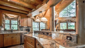 Une cuisine spacieuse dotée de meubles en bois, de plans de travail en granit et de grandes fenêtres offrant une vue sur la forêt environnante.