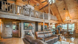 Un intérieur spacieux de chalet en bois, avec un plafond haut, un coin repas, une cuisine et un salon doté de canapés en cuir.
