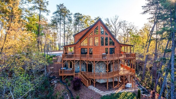 Une grande cabane en bois dotée de plusieurs terrasses et de grandes fenêtres, entourée d’une forêt dense.