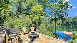 A patio with outdoor furniture, a fire pit, and a view of a lake surrounded by trees. - Shumont Lake Lakefront, Resort Access - All Decked Out by Carolina Properties (Lake Lure)