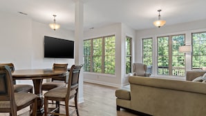 A spacious living room with a large window, a dining area with a TV, and a sofa. - Shumont Lake Lakefront, Resort Access - All Decked Out by Carolina Properties (Lake Lure)