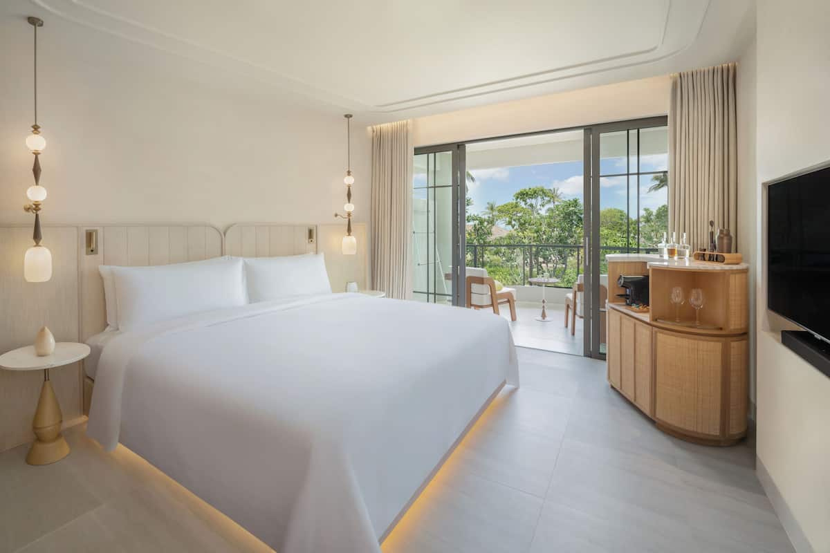 A hotel room with a large bed, a TV, a small table with a vase, and a balcony with a view.