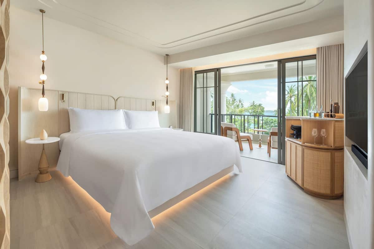 A hotel room with a large bed, a balcony with a view, a television, and a minibar.