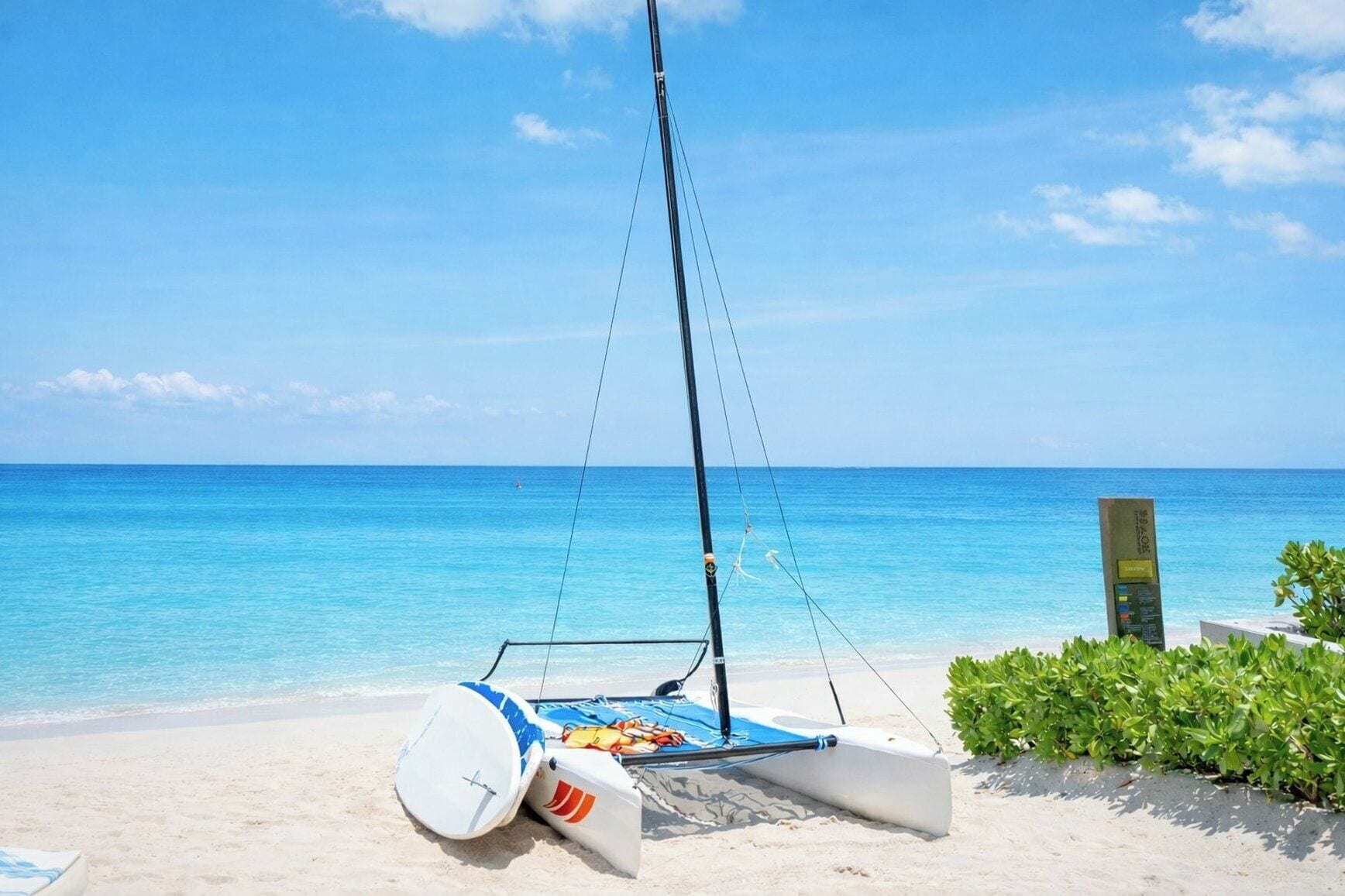 Un velero en una playa arenosa con aguas azules cristalinas y un horizonte lejano.